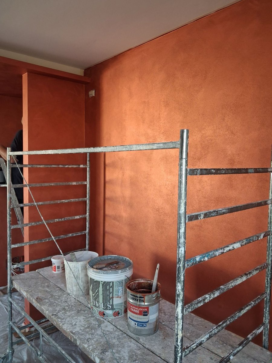 Wand mit dekorativer Gestaltung in Terrakotta während der Arbeiten, mit Rollgerüst und Farbeimern